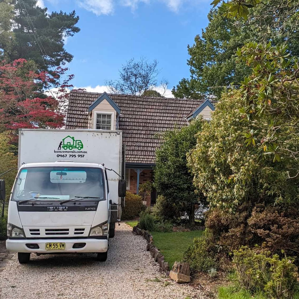 Bons Removals truck in the gravel driveway of a cottage with a leafy garden