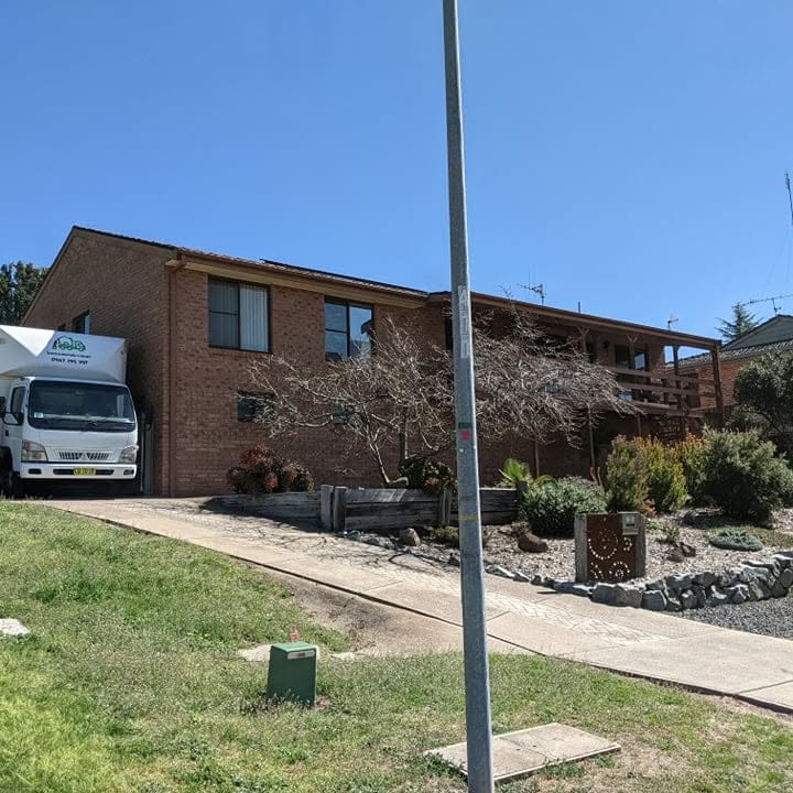 Bons Removals truck in the driveway of a brick home under a clear sky