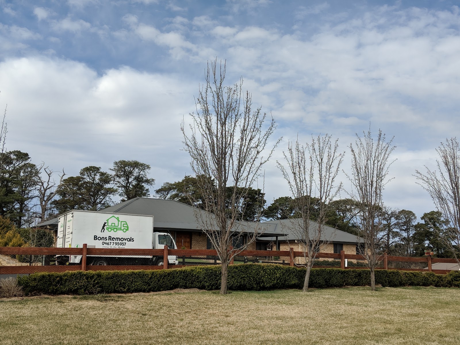 Bons Removals truck outside a brick house behind a hedge and bare winter trees