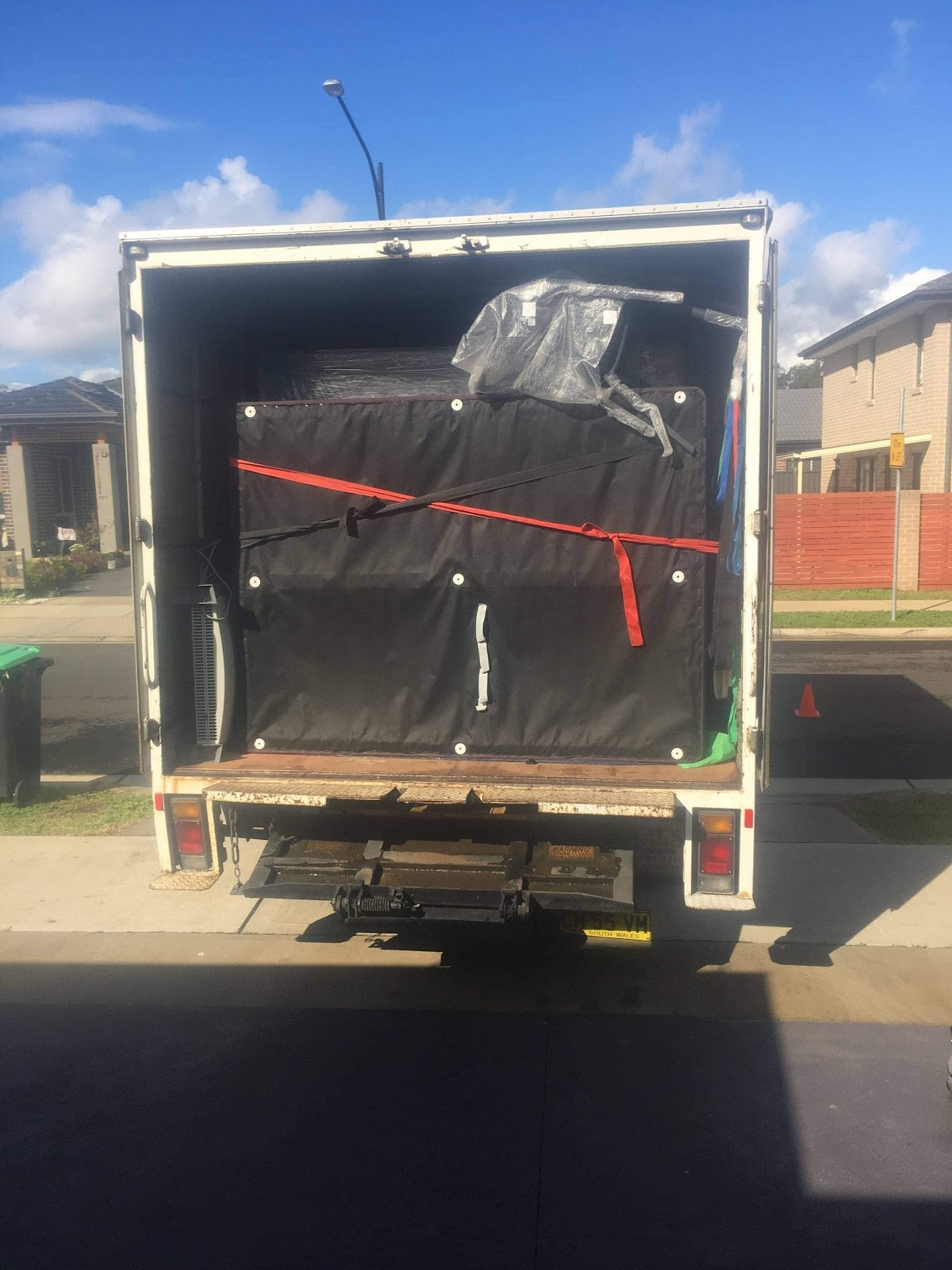 The back of a Bons Removals truck with a large wrapped item held by red straps