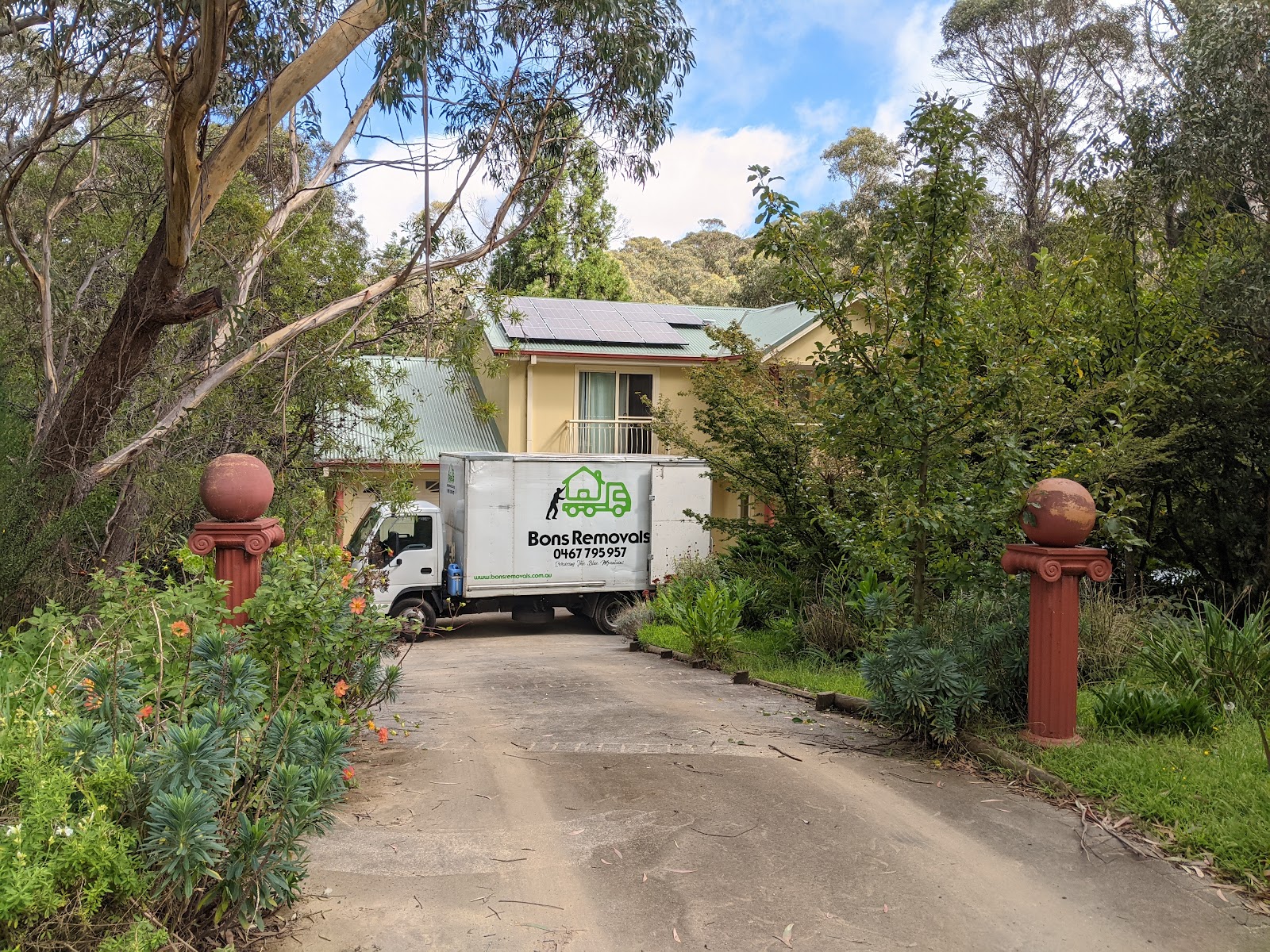 A Bons Removals truck backed into a steep bush driveway between two red gate pillars